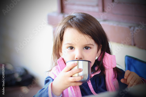 warmly dressed girl drinking from a metal cup outdoors
