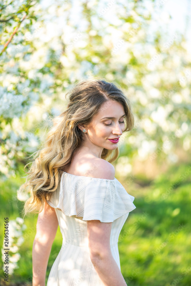 Woman in a blooming orchard at springtime. Enjoying sunny warm day. Retro style dress. Colorful spring moods Woman in a blooming orchard at springtime. Enjoying sunny warm day. Retro style dress. Colorful spring moods