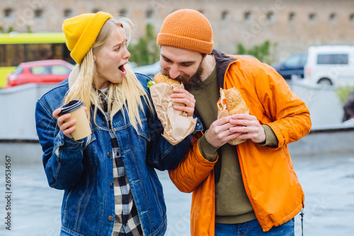 Hungry beard man taking croissants out of woman and biting it with greed at city street. I dont believe you. Shocked emotional blond woman try to give back, gazes with stupefaction. Reaction concept