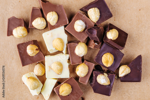Chunks of milk, white and dark chocolate with hazelnuts close-up. Photo in warm colors. Sweetness. World chocolate day
