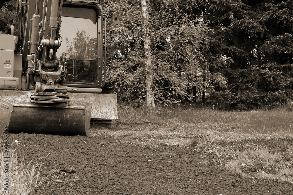 Small excavator in garden doing landscaping. Monochrome image with copy space.