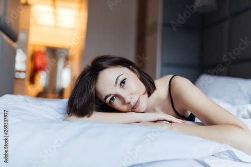 Beautiful young woman looking at camera while lying on the bed at home