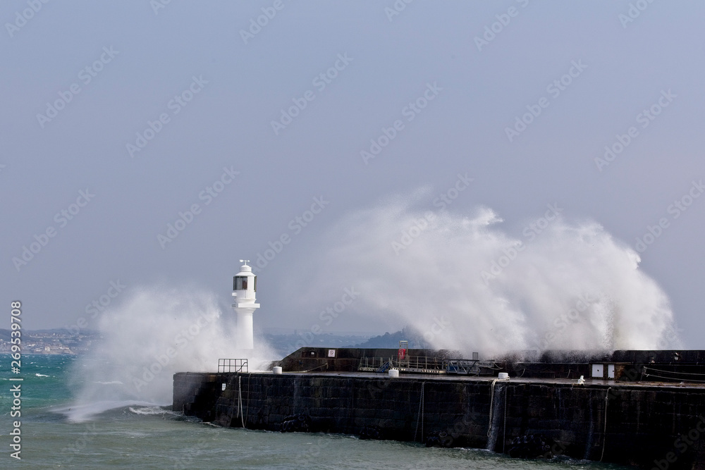 Waves breaking over Penzance's harbour wall and lighthouse, Cornwall, England, UK.