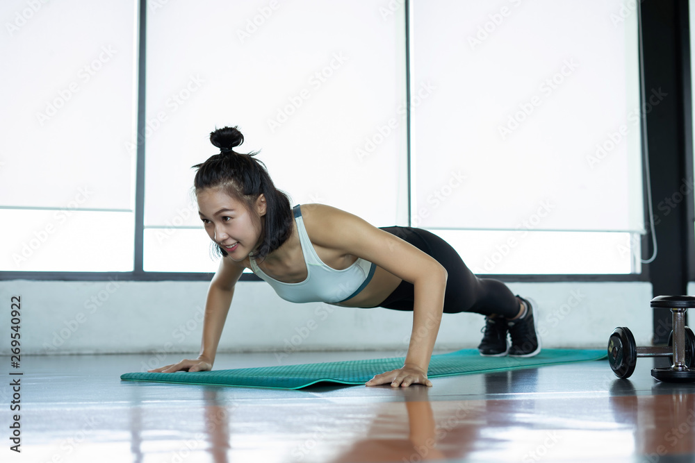 Obraz premium Woman doing fitness training. Fitness woman doing push ups on a training mat. young woman doing push-ups at the gym. Muscular female doing pushups on exercise mat at gym.