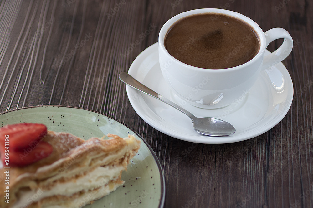A piece of cake handmade with custard and a cup of coffee on a brown table. A piece of cake handmade with custard and a cup of coffee on a brown table.