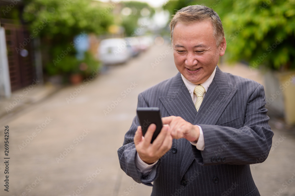 Mature Asian businessman using mobile phone in the streets outdo Mature Asian businessman using mobile phone in the streets outdo
