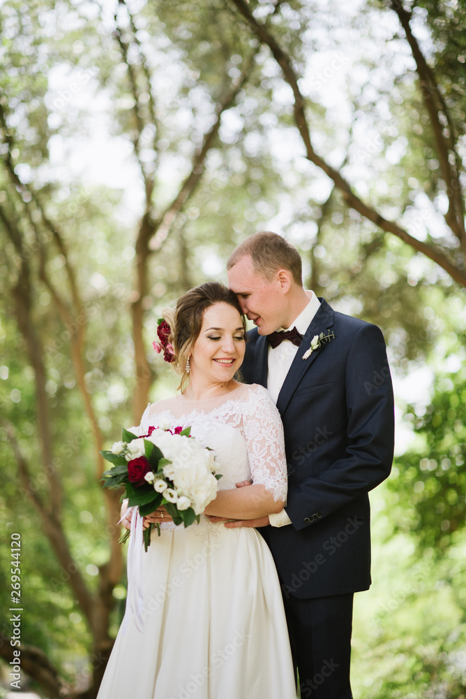 The groom in a suit and the bride in a wedding dress are walking in the park The groom in a suit and the bride in a wedding dress are walking in the park