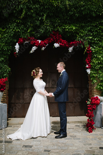 The groom in a suit and the bride in a wedding dress are standing at the wedding arch at the wedding ceremony