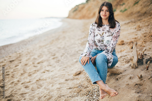 Stylish hipster girl sitting on beach at sea. Happy fashionable boho woman relaxing at sandy cliff on tropical island and looking at water. Travel and summer vacation. Space for text © sonyachny