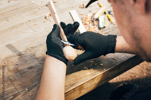 Wooden workshop. Hands carving spoon from wood, working with chisel close up. Process of making wooden spoon, chisel, pencil, compass, ruler on dirty table with shavings photo