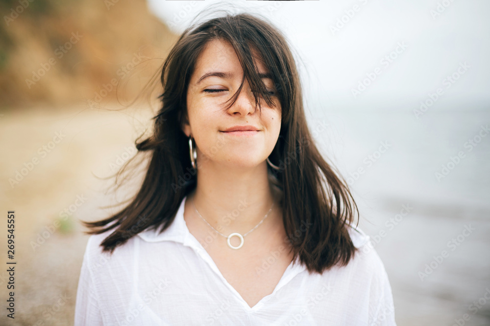Stylish hipster girl relaxing on beach. Summer vacation. Portrait of  happy boho woman enjoying time and smiling at windy sea. Space for text. Calm moment.