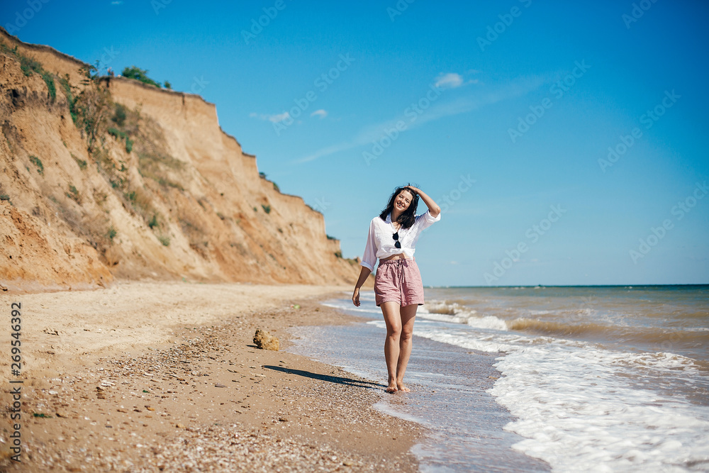 Stylish hipster girl relaxing on beach and having fun.  Happy young boho woman walking and smiling in sea waves in sunny warm day on tropical island. Summer vacation. Space for text