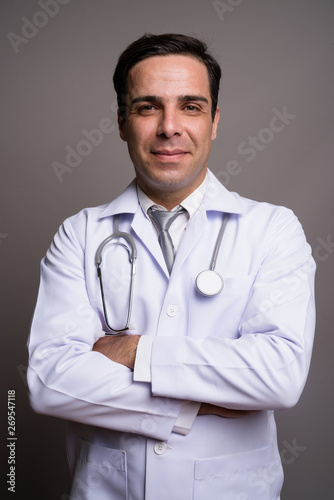 Handsome Persian man doctor against gray background