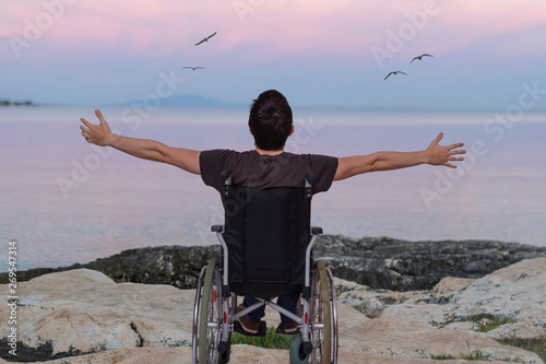 Disabled man on wheelchair near beach at sunset.