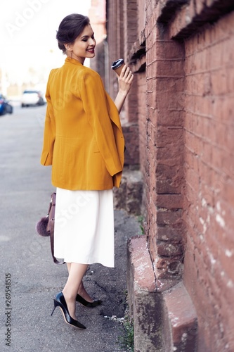 Portrait fashion woman walking on street . She wears yellow jacket, smiling to side.