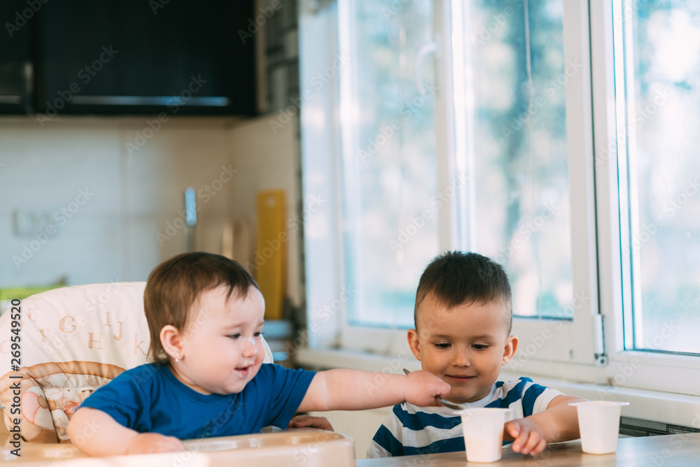 Children brother and sister in the kitchen eating yogurt on their own Children brother and sister in the kitchen eating yogurt on their own