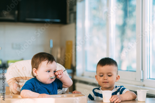 Children brother and sister in the kitchen eating yogurt on their own