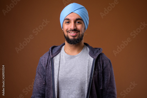 Foto Young bearded Indian Sikh man wearing turban against brown backg