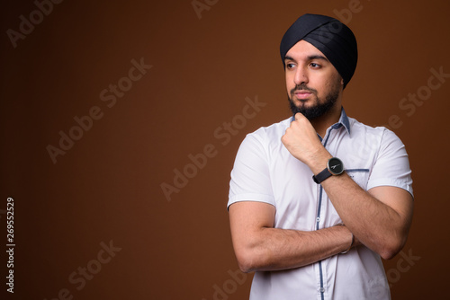 Canvas Print Young bearded Indian Sikh man wearing turban against brown backg