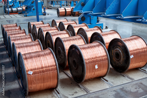 Several rows of new finished coils with copper wire in the production shop. Copper wire is wound on metal coils or drums. Modern line of automatic production of electric cable and wire.