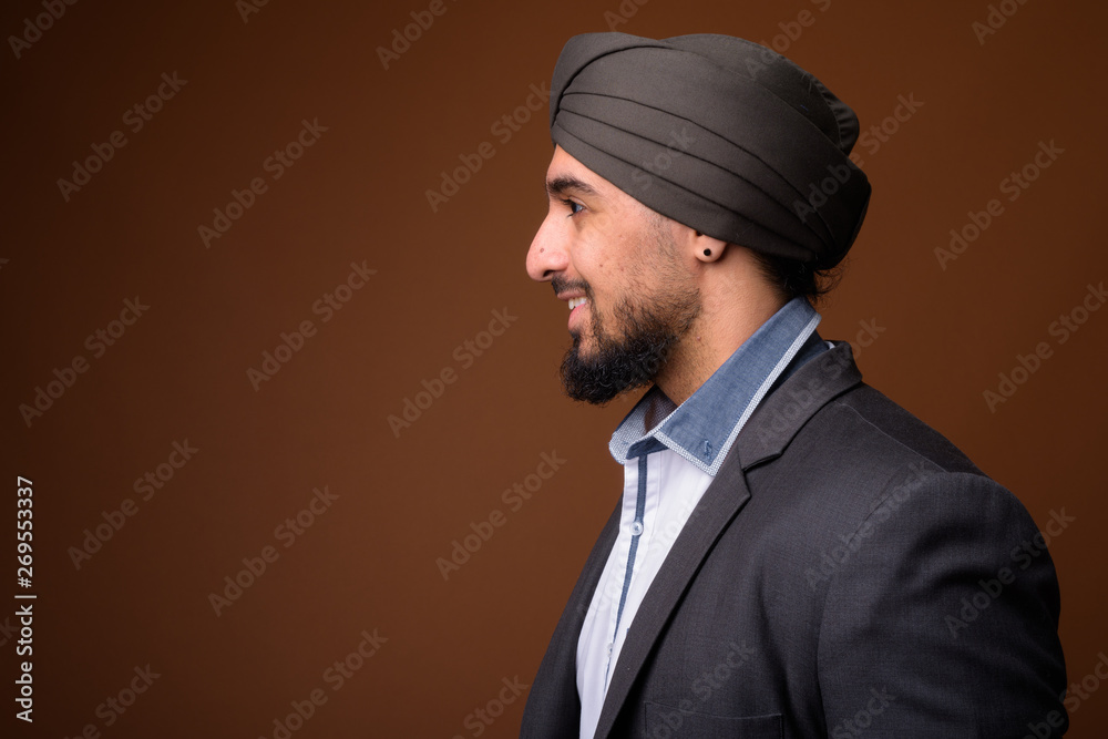 Young bearded Indian Sikh businessman wearing turban against bro Young bearded Indian Sikh businessman wearing turban against bro