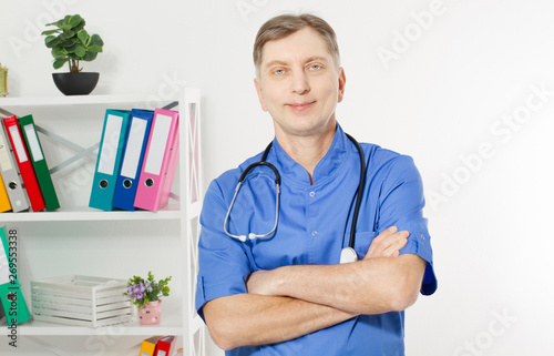 Portrait Of A Confident Mature Doctor Looking At Camera Isolated On Medical Office Background.