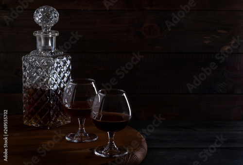 Brandy or cognac in glasses and a decanter on a brown wooden background