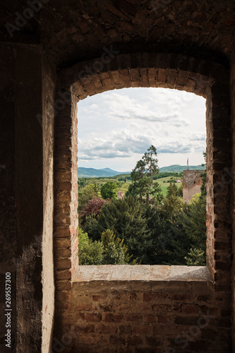 view through old medieval window of landscape in a sunny day with forest mountains and clouds