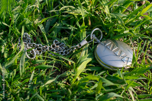 Vintage pocket watch in closed form lie on the green grass. The clock mechanism is not visible. Sunny summer day