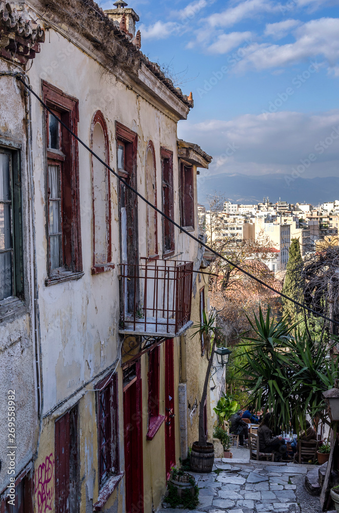 Naklejka premium Plaka, Athens / Greece - January 19, 2016: Old traditional abandoned house in a narrow alley in the historical area of Plaka below Acropolis, viewing the center of Athens. Sunny day, cloudy sky