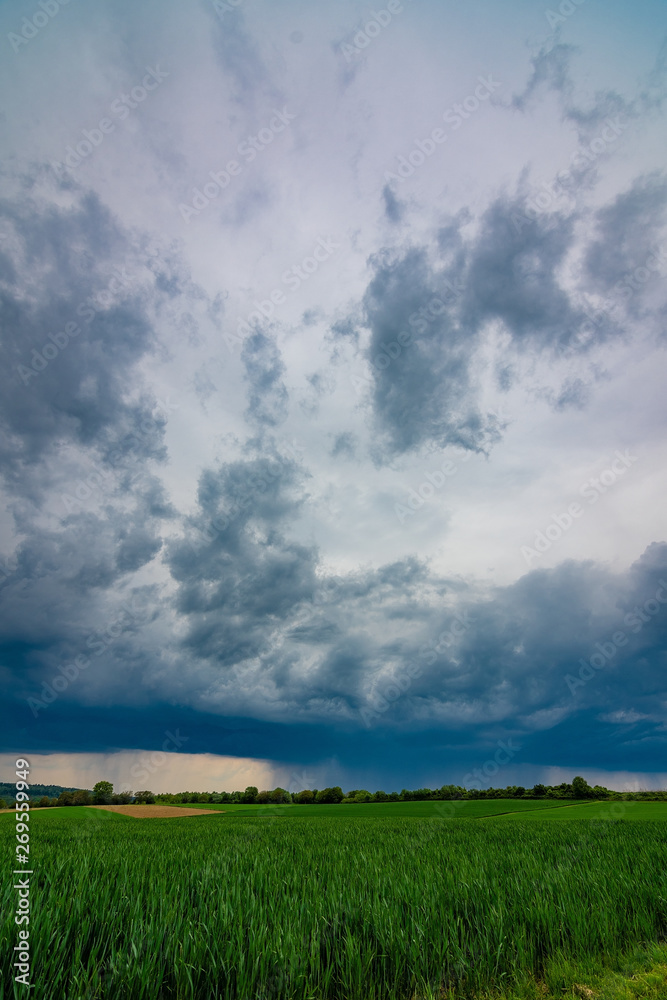 The green fields with the dark, stormy clouds in the background The green fields with the dark, stormy clouds in the background