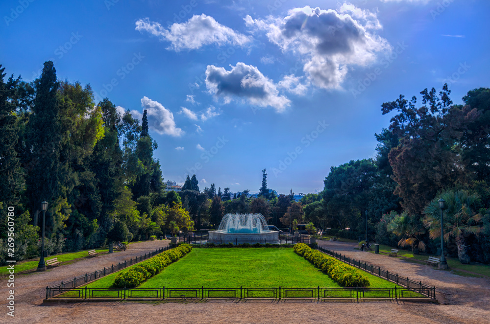 Athens, Attica / Greece. The garden with the marble fountain in front of the Zappeion Hall neo-classical building in the National Garden near Syntagma Square. Sunny day, cloudy sky, nobody