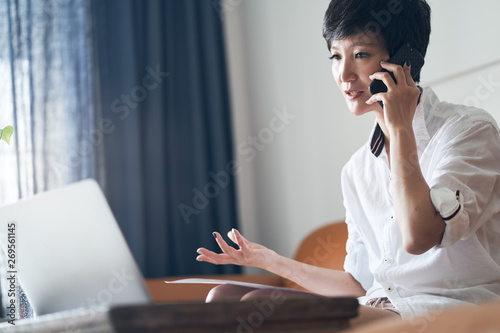 Photography Asian self employed woman sitting on couch  & talking on phone while working on