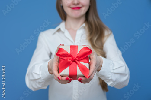 Woman in white shirt, holding a box with a gift with a red ribbon, front view, close up