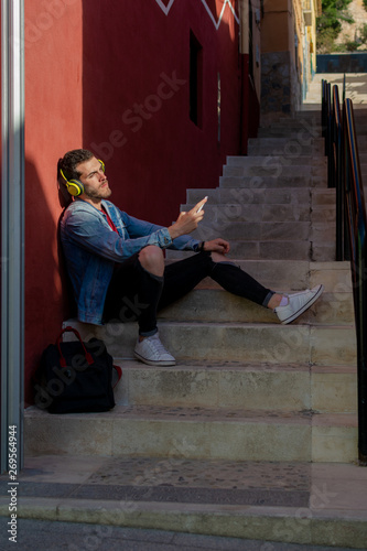 Outdoor portrait of modern young man with smart phone sitting in the street