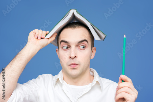 Guy, student, white shirt with, open book on his head, having idea and pointing up, inside, smiling, close up