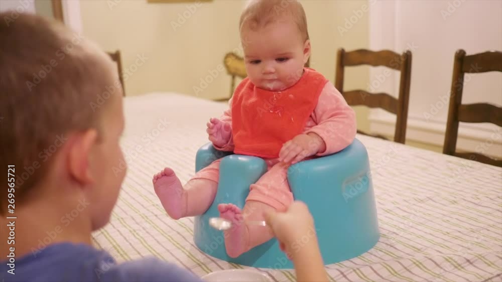 Toddler boy feeds his baby sister dinner at the table Toddler boy feeds his baby sister dinner at the table