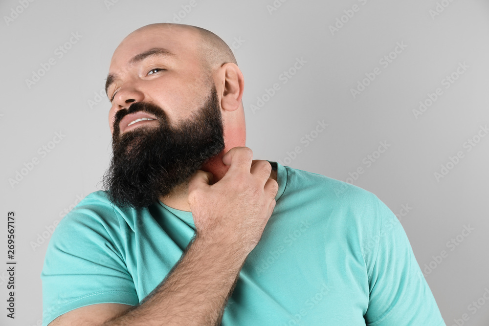 Man with allergy symptoms scratching neck on grey background Man with allergy symptoms scratching neck on grey background