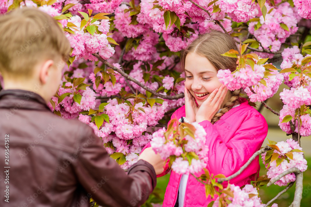 Romantic teens. Kids enjoying pink cherry blossom. Tender bloom. Couple kids on flowers of sakura tree background. Little girl enjoy spring flowers bouquet. Giving all flowers to her. Surprising her