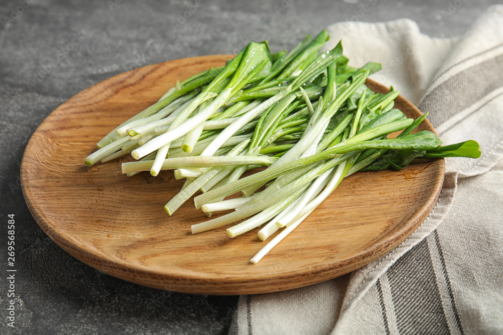 Wooden plate with wild garlic or ramson on grey table