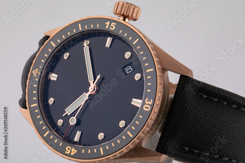 Golden wristwatch with black dial, phosphor clockwise with chronograph on black cloth strap isolated on white background.