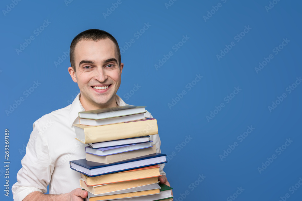 Attractive man in the white shirt with books, smiling, looking at the camera, close up, the concept of heavy loads in education, blue background, copy space Attractive man in the white shirt with books, smiling, looking at the camera, close up, the concept of heavy loads in education, blue background, copy space