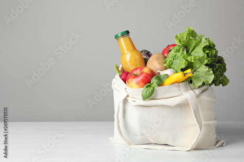 Cloth bag with vegetables and bottle of juice on table against grey background. Space for text