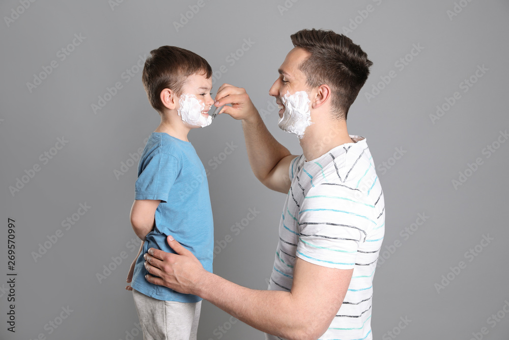 Dad pretending to shave his little son on color background