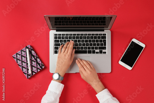 Woman using modern laptop at color table, top view