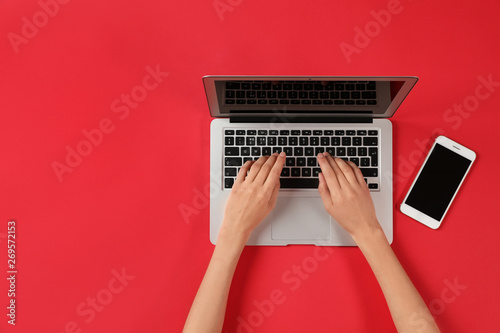 Woman using modern laptop at color table, top view