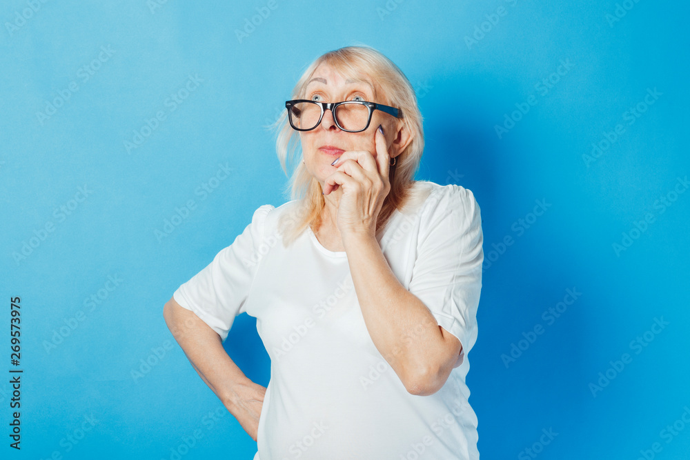 Old woman with a pensive face on a blue background. Concept of dreams, plans for the future, thinking about something