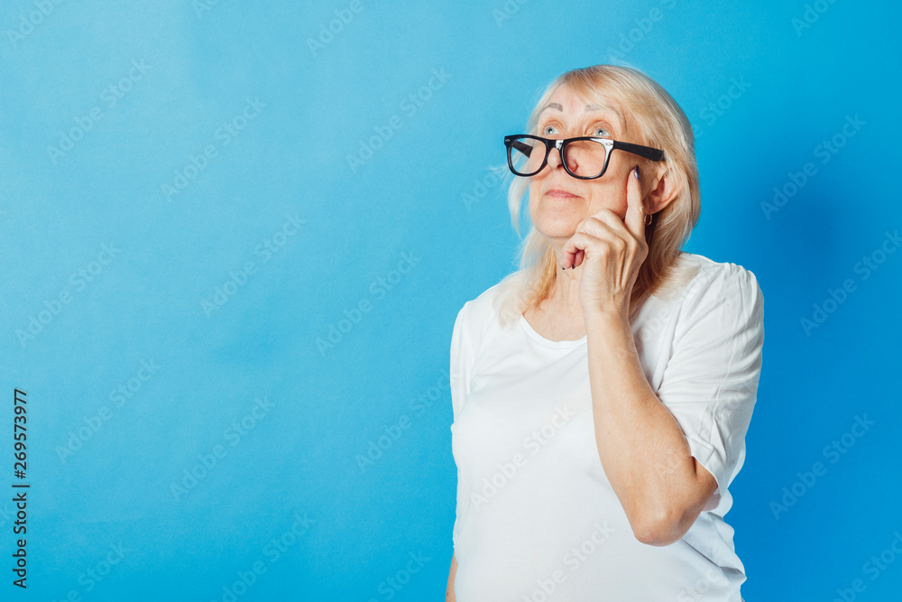 Old woman with a pensive face on a blue background. Concept of dreams, plans for the future, thinking about something Old woman with a pensive face on a blue background. Concept of dreams, plans for the future, thinking about something