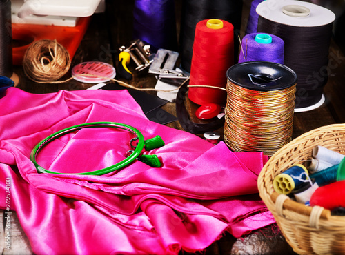 Seamstress group object red and gold sewing spool and embroidery hoop with basket on pink textile material. photo