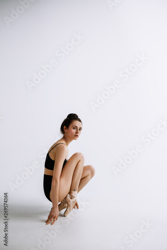Fashion ballet. Young female ballet dancer in black bodysuit against white studio background. Caucasian ballerina like a fashion model. Style, contemporary choreography concept. Creative art photo.